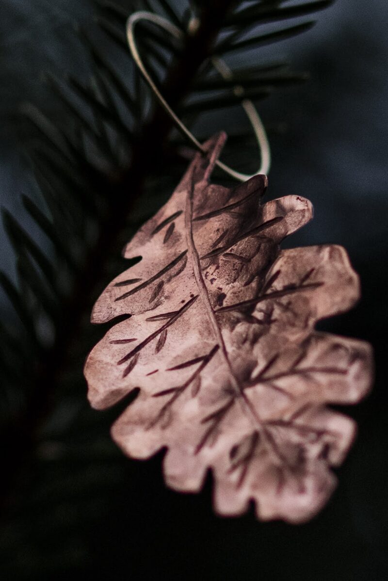 A picture of a copper earring shaped as an oak leaf.